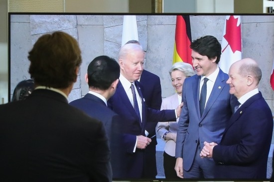 2022年3月24日，在比利時布魯塞爾的北約總部，一名男子觀看屏幕上美國總統(tǒng)拜登（右四）、歐盟委員會主席馮德萊恩（右三）、加拿大總理特魯多（右二）、德國總理朔爾茨（右一）出席七國集團(tuán)峰會合影儀式的畫面。新華社記者鄭煥松攝