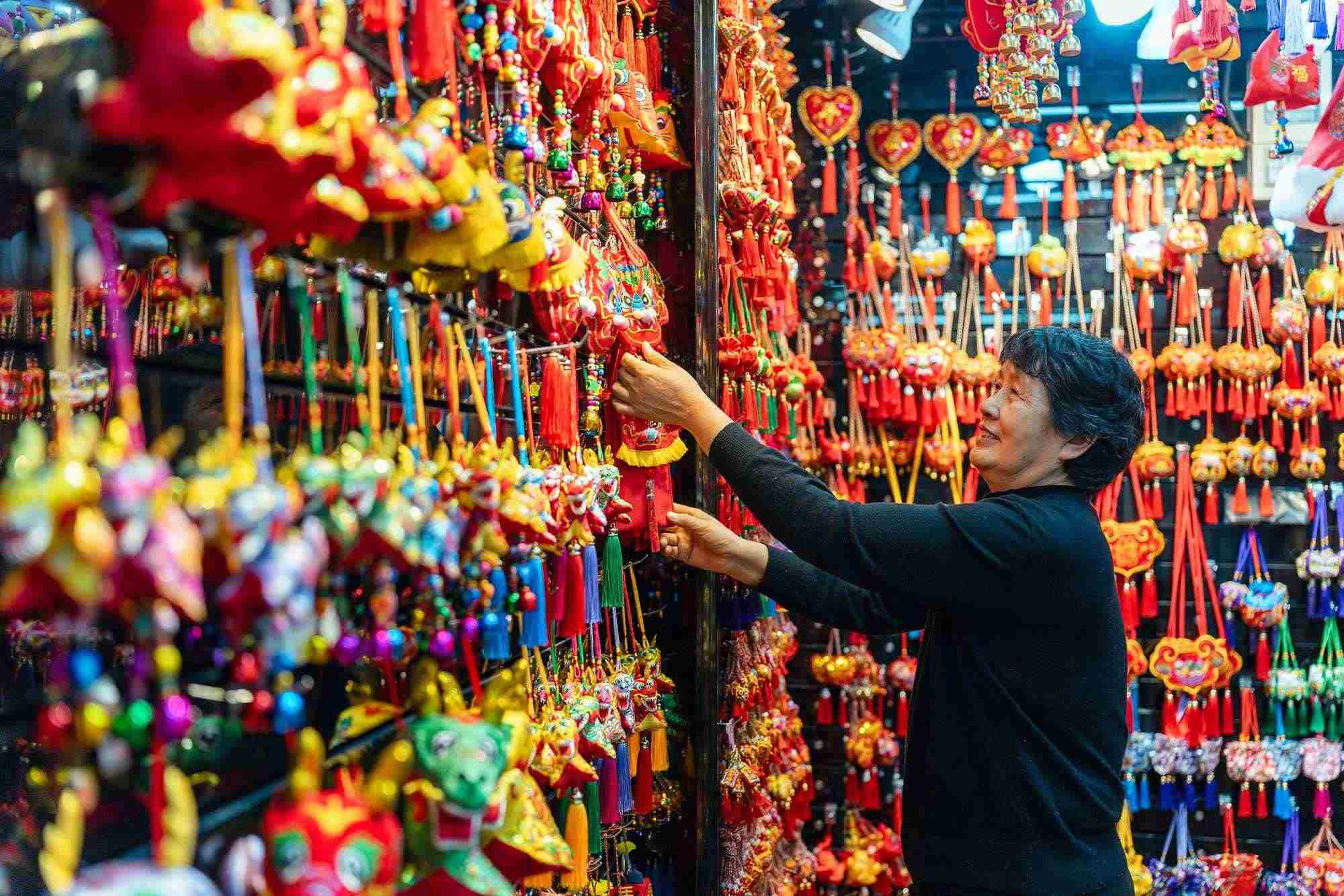 2023年12月11日，金華義烏國際商貿(mào)城，龍年喜慶用品掛滿攤位，顧客正在挑選中。