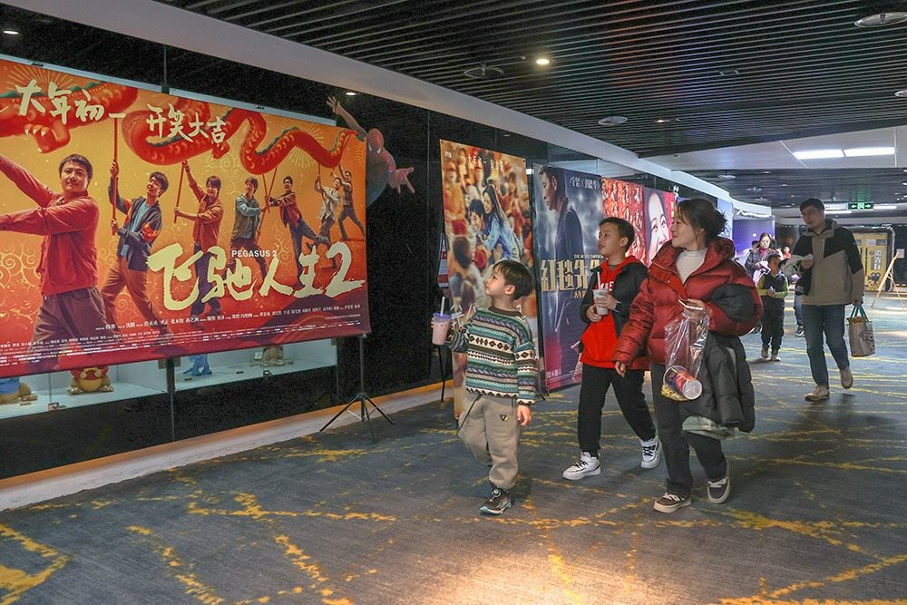 △ 2024年2月16日，在江西贛州一家電影院，觀眾從春節(jié)檔電影的宣傳展板前走過。
