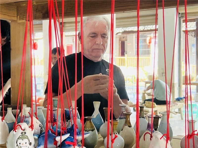 鄉(xiāng)愁如同一根根紅線，將游子與故鄉(xiāng)永遠(yuǎn)地牽連到一起?；逄账囄幕瘎?chuàng)意一條街的母氏陶藝館內(nèi)，紅線吊著陶瓶，思緒游走萬里。摩爾多瓦“信息標(biāo)簽”通訊社社長(zhǎng)亞歷山大·塔納斯端詳著館內(nèi)展示的陶藝作品，并挑選出心儀的小擺件帶回摩爾多瓦，也帶走花茂村的“鄉(xiāng)愁”。（張亞欣攝）
