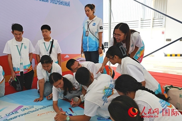 泰國學(xué)生在開營儀式展板上繪制圖案。人民網(wǎng)記者 白元琪攝