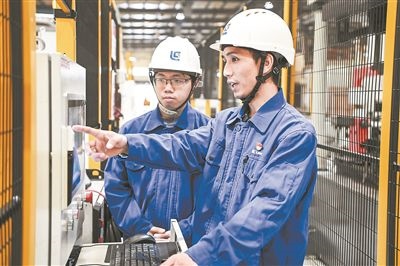 在廣西柳工機械股份有限公司生產(chǎn)車間內(nèi)，一名高級技師（右）給徒弟講解數(shù)控設備操作細節(jié)。新華社記者 曹祎銘攝